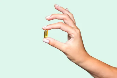 Mão segurando um comprimido com o indicador e o polegar