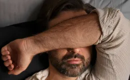 Homem deitado com o braço cobrindo o rosto, representando dificuldade para dormir e sintomas comuns de insônia.