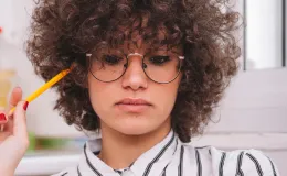 Mulher distraída com lápis no rosto enquanto trabalha, representando dificuldades de concentração associadas ao TDAH.