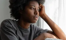 Mulher olhando pela janela com expressão pensativa, representando sentimentos de ansiedade e preocupação.