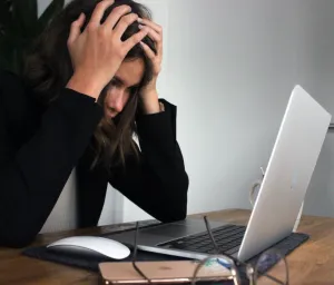 Mulher em frente ao notebook/laptop com as duas mãos na cabeça numa expressão de estresse