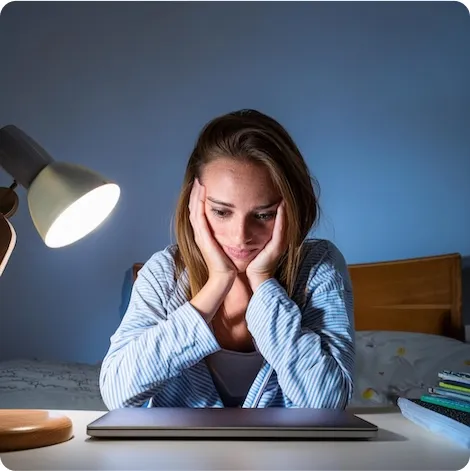 Mulher sentada à noite, parecendo preocupada em frente a um laptop.
